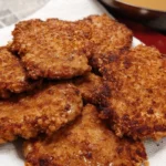Fried cubed steak stacked on a plate with crispy golden breading and homemade gravy in the background.